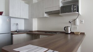 Una cocina moderna con armarios blancos, un refrigerador de acero inoxidable, un microondas y una tetera sobre la encimera.