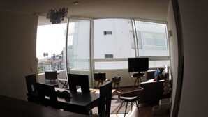Una habitación con una mesa de comedor, sillas, un televisor sobre un mueble bajo y un amplio ventanal con vistas a edificios y palmeras.