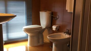 A bathroom with a toilet, bidet, sink, and a towel on a bench.