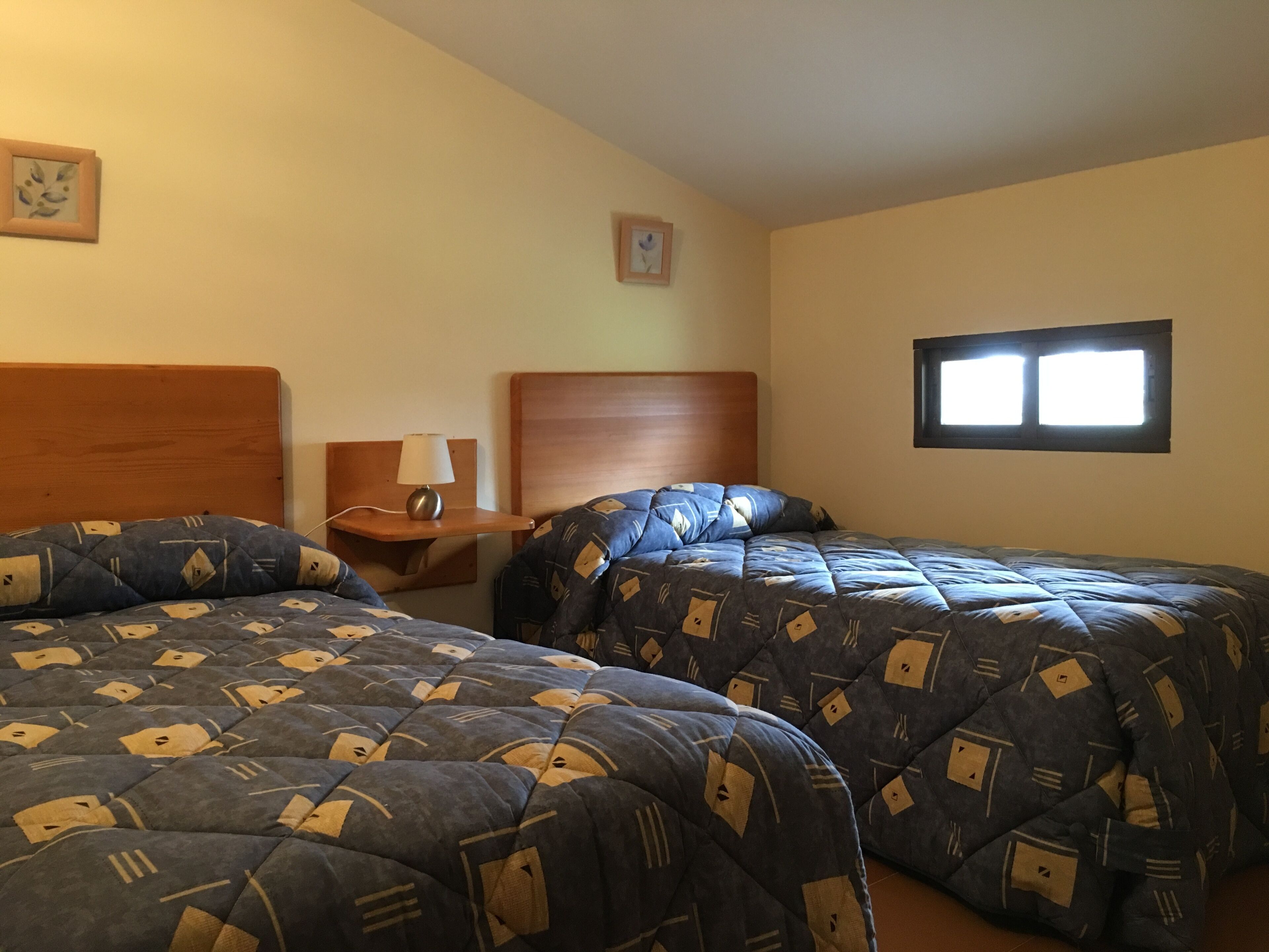 Habitación de hotel con dos camas, una mesita de noche, una lámpara y una ventana.