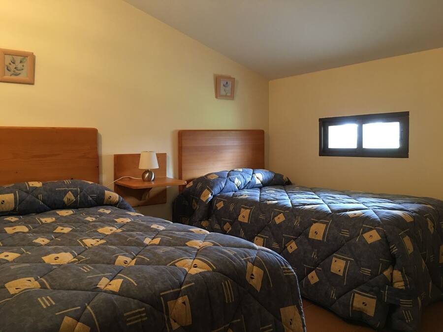 A hotel room with two beds, a nightstand, a lamp, and a window.