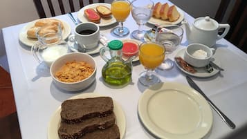 Une table de petit-déjeuner avec divers aliments et boissons, notamment du pain, des céréales, du jus de fruits et une théière.