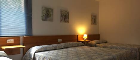 A hotel room with two beds, a nightstand with a lamp, and wall art.