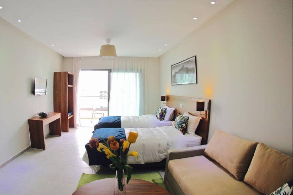 A hotel room with a large bed, a sofa, a desk, and a chair. There is a window with curtains and a painting on the wall.