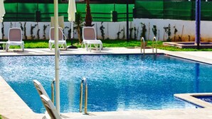 Una piscina con sillas de descanso blancas y una pared verde al fondo.