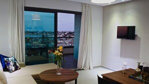 Una sala moderna con un sofá, una mesa de centro con un florero, una mesa de comedor con un juego de té y un televisor montado en la pared.