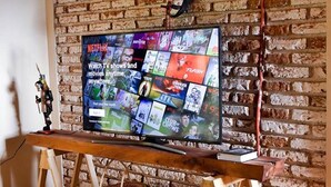 Un televisor montado en una pared de ladrillo con un soporte de madera, mostrando la interfaz de Netflix.