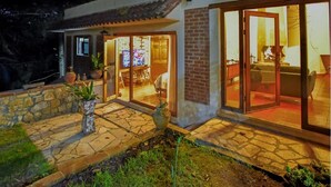 Una casa con un patio de piedra, una chimenea y un amplio ventanal que da a una sala de estar.