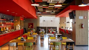A modern restaurant interior with red walls, colorful ceiling panels, and a variety of seating arrangements including tables and booths. - ibis Mazatlán Marina (Mazatlán)