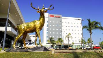 Una statua dorata di un cervo davanti a un hotel con diversi piani e una palma sullo sfondo.