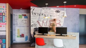 Un espacio de oficina moderno con un escritorio central, dos monitores de computadora y un gran mural en la pared con diversos textos y diagramas.