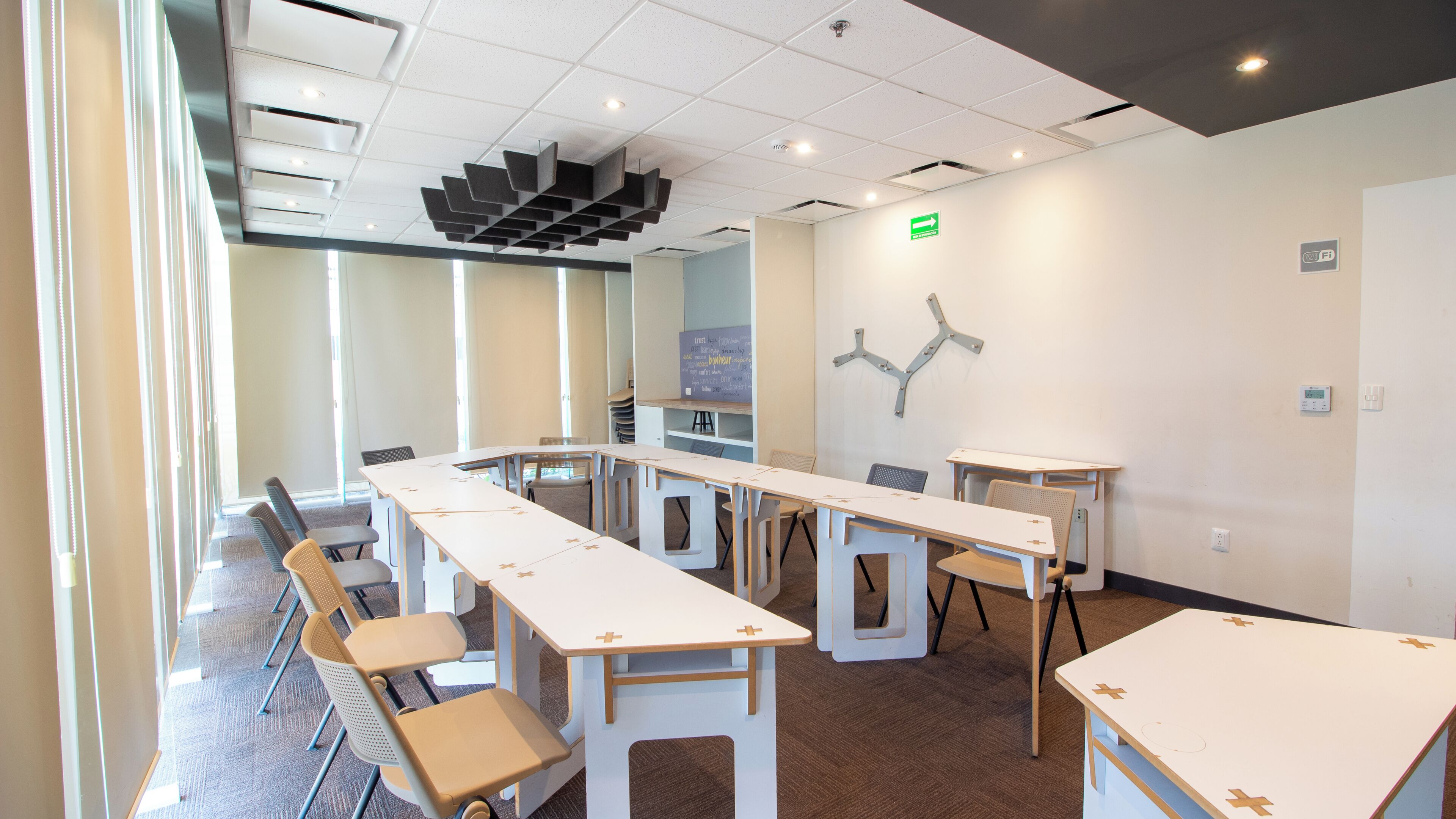 Une salle de conférence avec des tables et des chaises blanches, un tableau blanc et un luminaire fixé au mur.