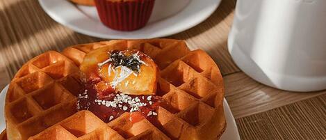 Ein Waffel mit Belag, ein Muffin und eine Kaffeetasse auf einem Holztisch.