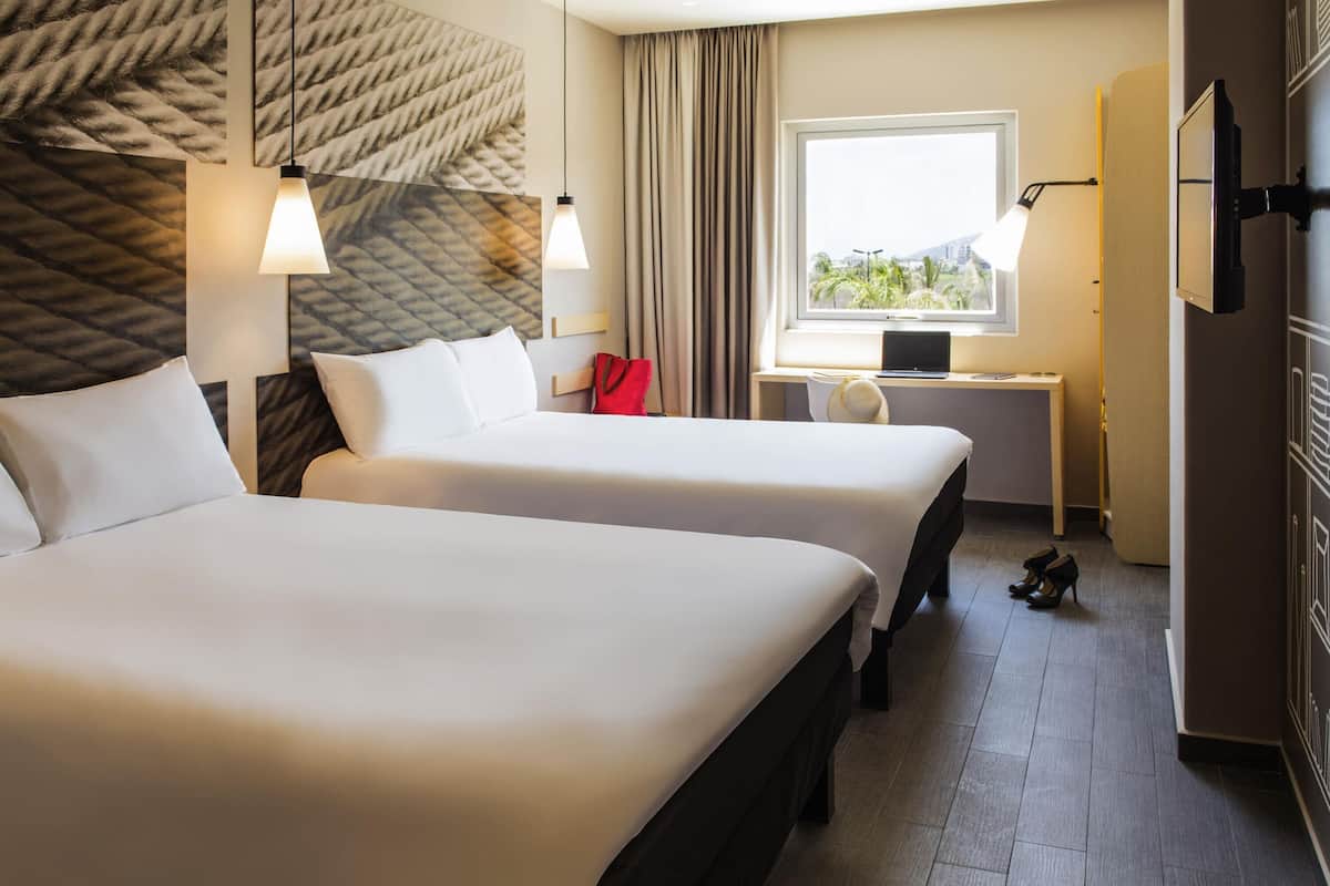 A hotel room with two beds, a desk with a computer, a TV, and a window with a view.