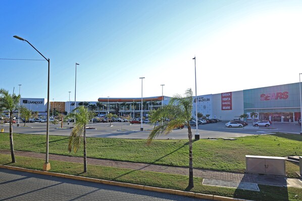 A parking lot with a large building in the background, a grassy area with palm trees, and a clear sky. - ibis Mazatlán Marina (Mazatlán)