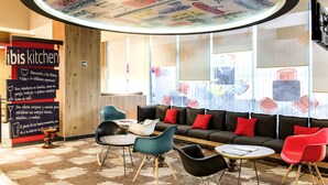 Un interior moderno con un diseño de techo circular, una zona de estar con sofás y sillones, y un cartel que indica 'ibis kitchen'.