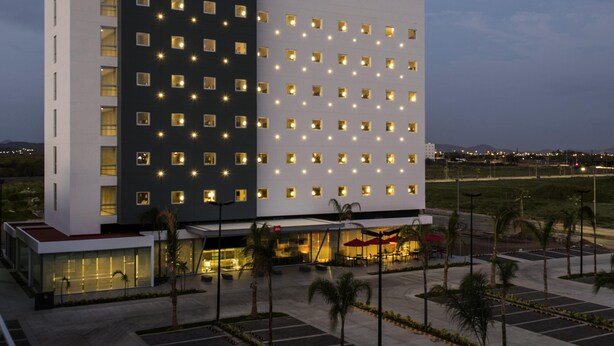 Un hotel moderno con un llamativo letrero de 'ibis HOTEL', un amplio estacionamiento y una entrada bien iluminada.