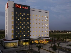 A modern hotel with a prominent 'ibis HOTEL' sign, a large parking area, and a well-lit entrance. - ibis Mazatlán Marina (Mazatlán)