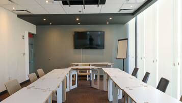 Een vergaderruimte met een grote tafel, stoelen, een scherm en een whiteboard.