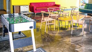 Ein hell erleuchteter Raum mit gelber Wand, einem roten Sofa und einem Kicker.