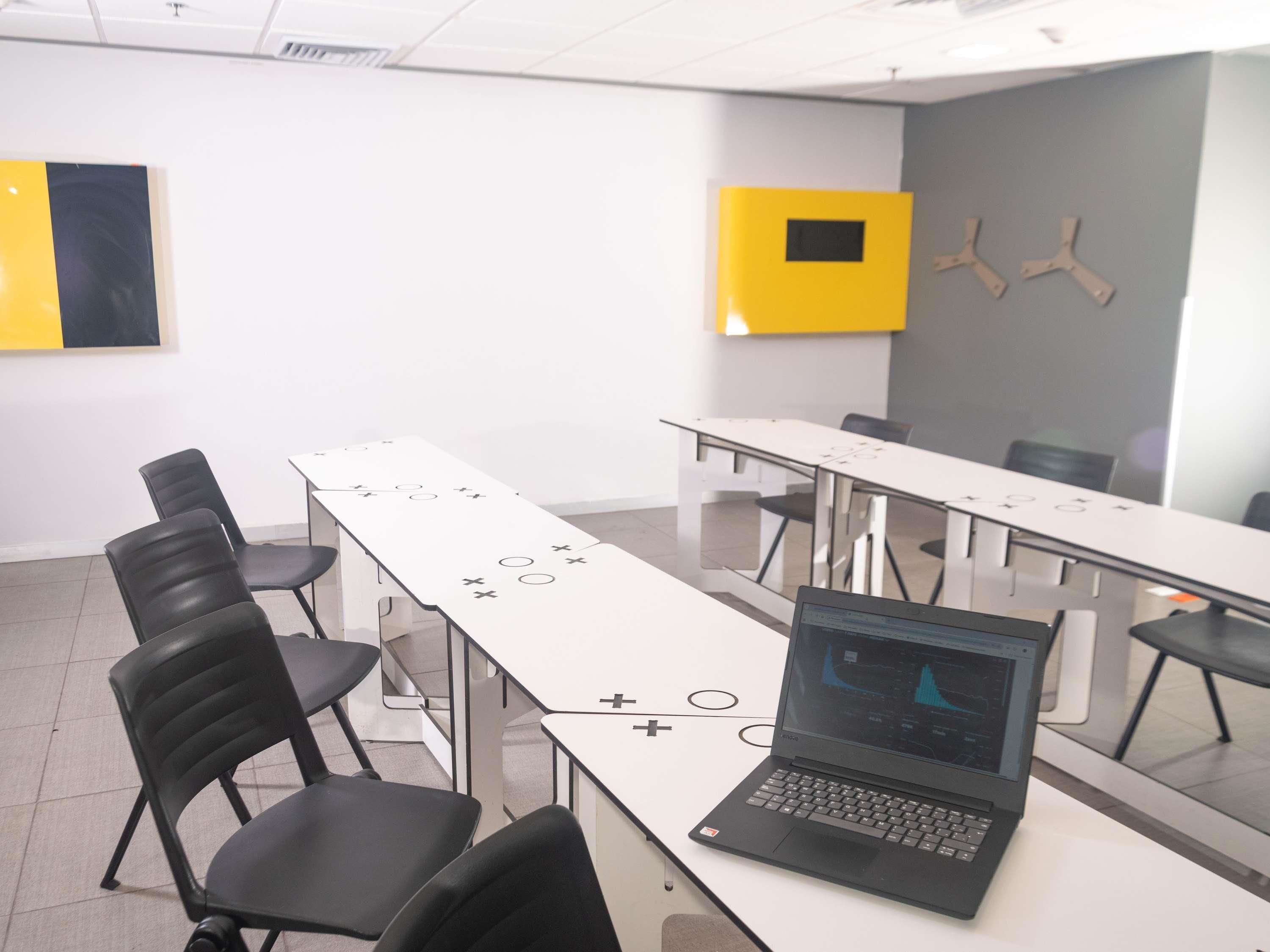 A conference room with a laptop on a table, black chairs, and a whiteboard.
