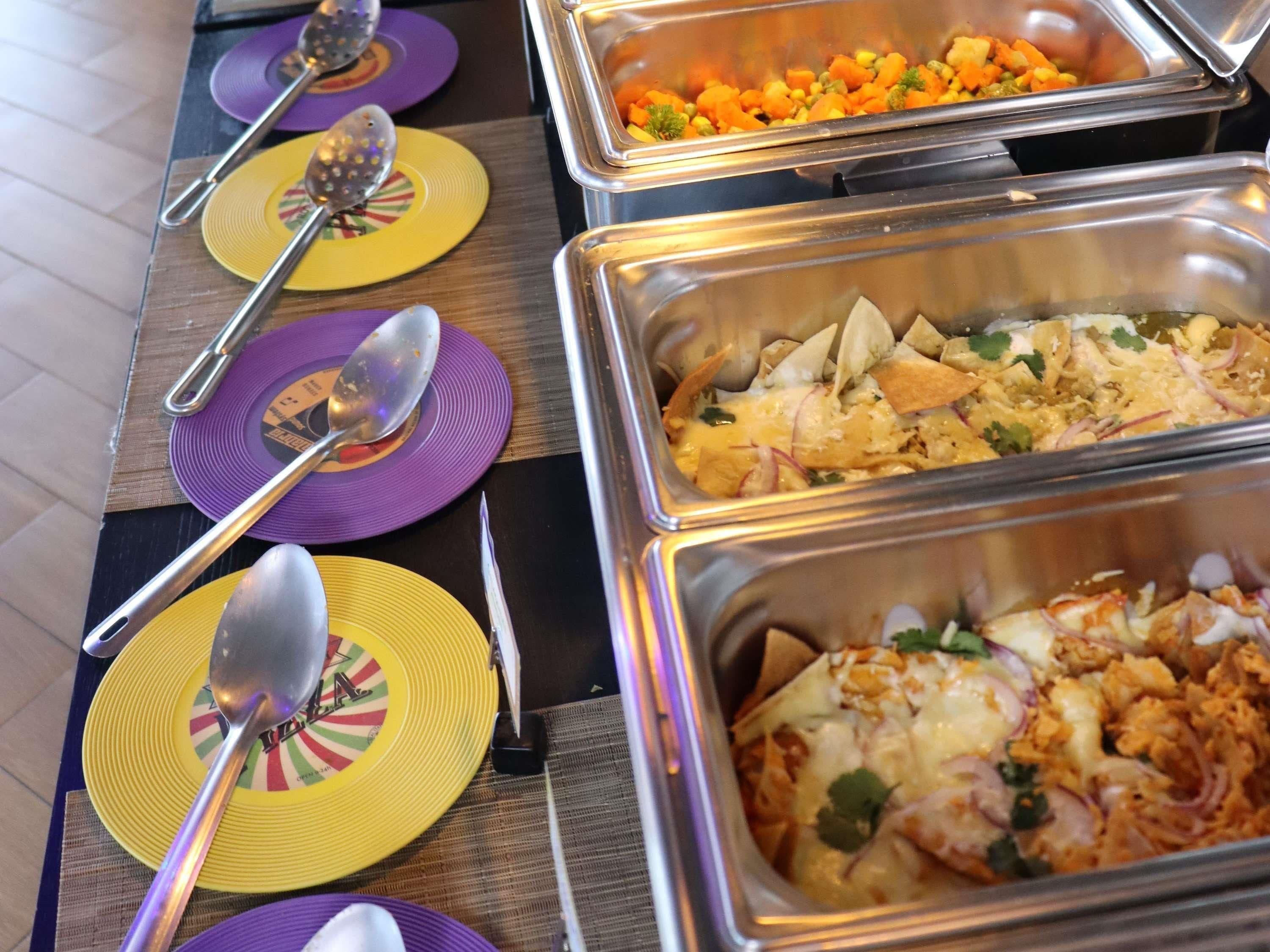 Un bufé con diversos platos, entre ellos, una ensalada, arroz y un pastel de carne, servidos en bandejas metálicas.