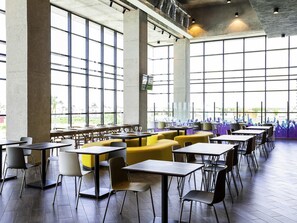A spacious indoor area with large windows, multiple tables and chairs, and a view of the outdoors. - ibis Styles Merida Galerias (Mérida)