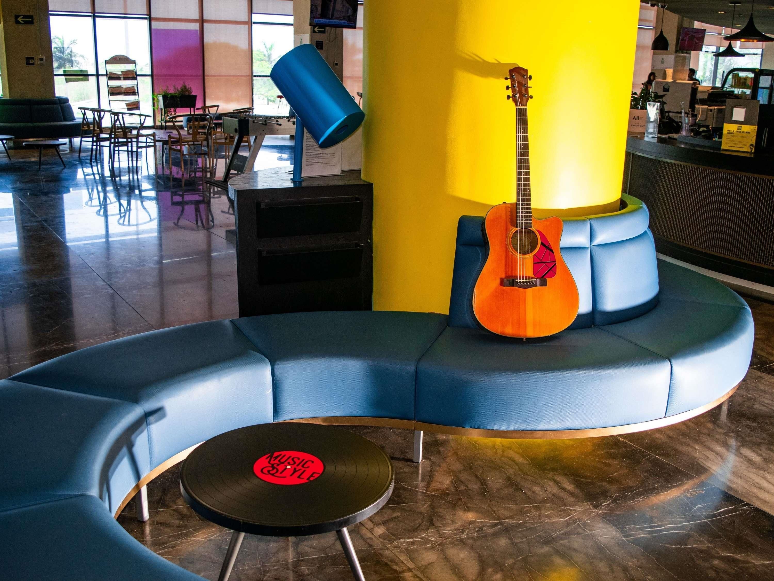 Un rincón de descanso con asientos azules en curva, una guitarra y un disco de vinilo sobre un taburete.
