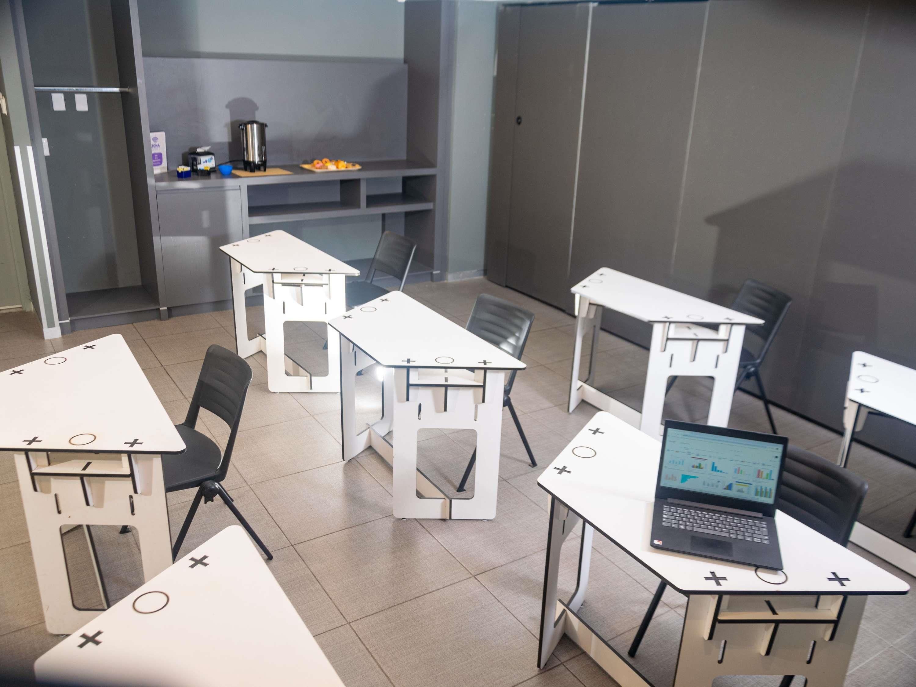 A modern room with white tables, chairs, and a laptop on one table.