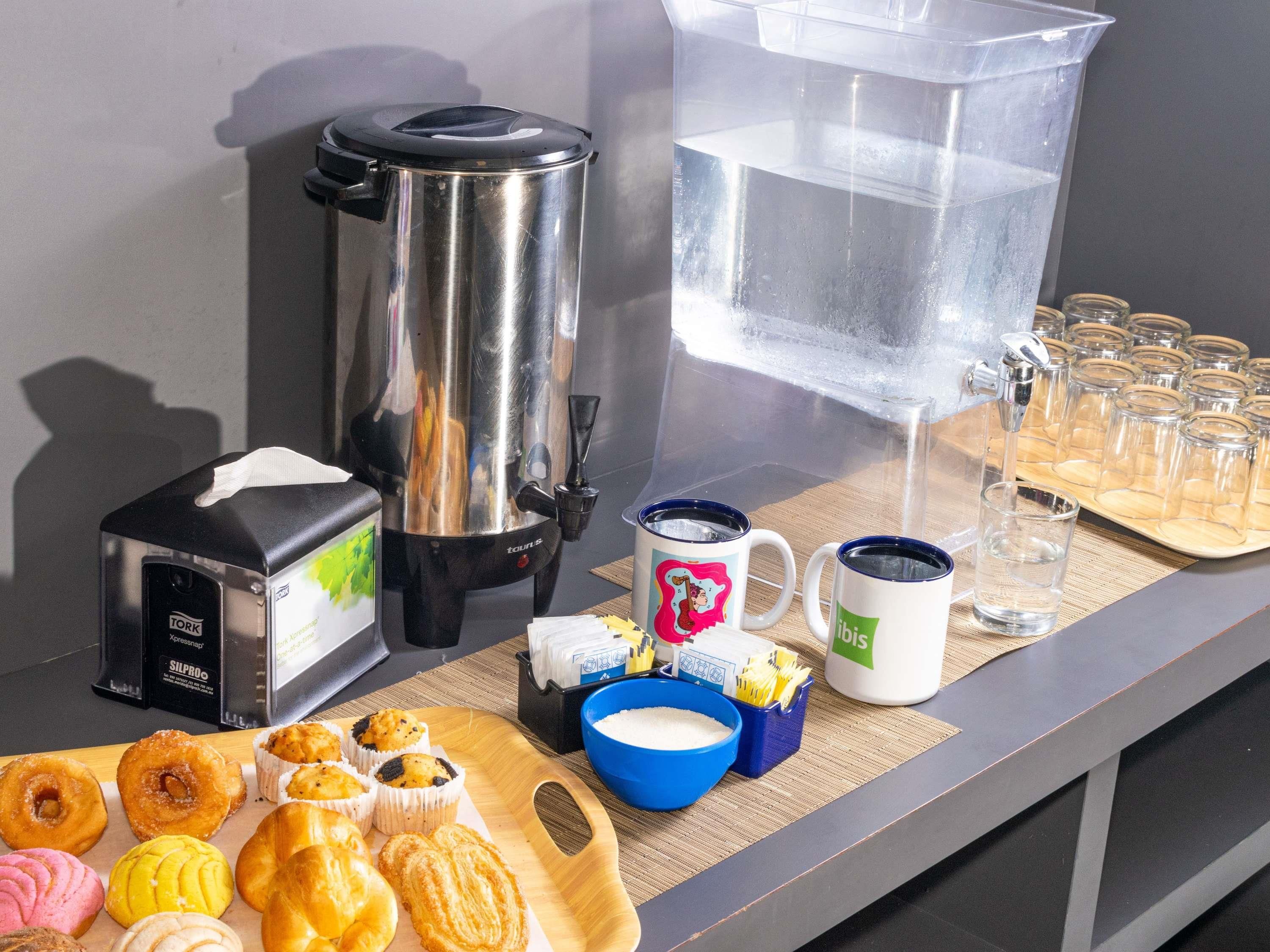 A breakfast setup with a coffee maker, a water dispenser, and a tray of pastries.