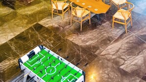 Un espacio interior luminoso con un sofá rojo, sillas de madera, una mesa de fútbol y una zona de asientos azules en círculo.