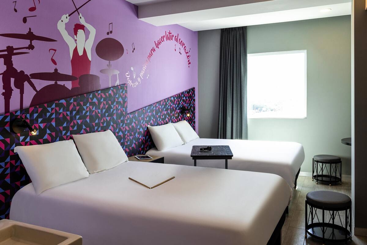Ein Hotelzimmer mit zwei Betten, einer Wandmalerei, einem Fenster und einem kleinen Tisch.