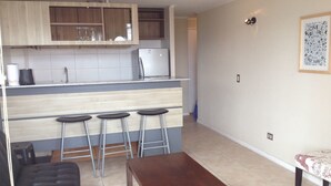 Een compacte woonruimte met een kitchenette, een eethoek met krukken en een bank.