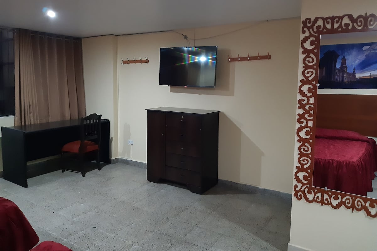 A living room with a TV mounted on the wall, a dark wooden cabinet, a red sofa, and a patterned wall decoration.