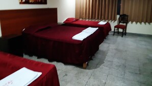 Quarto de hotel com três camas, cabeceira de madeira, um quadro na parede e uma cadeira.