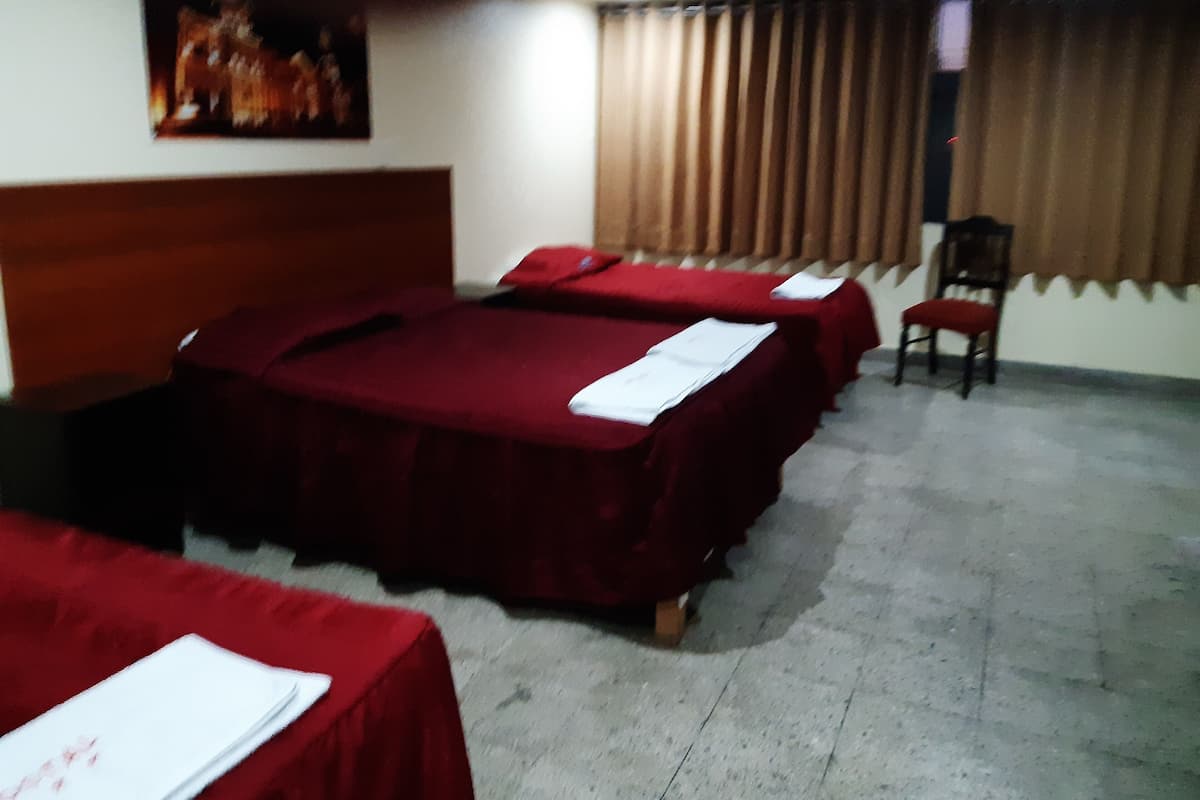 A hotel room with three beds, a wooden headboard, a painting on the wall, and a chair.