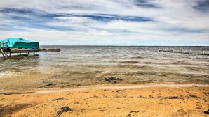 A beach with clear water, a dock, and a covered area. - Cozy Houghton Lake Vacation Rental w/ Fireplace! (Houghton Lake)