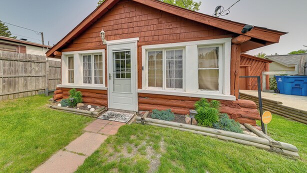 A wooden cabin with a front door, two windows, and a small porch area. - Cozy Houghton Lake Vacation Rental w/ Fireplace! (Houghton Lake)