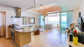 A modern kitchen with a central island, a dining area with a view, and a living space with a large window overlooking the ocean.
