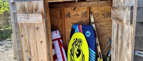 A wooden structure with a sign that reads "Help Yourself!" and various items including a yellow surfboard, a blue and red board, and a white bag.