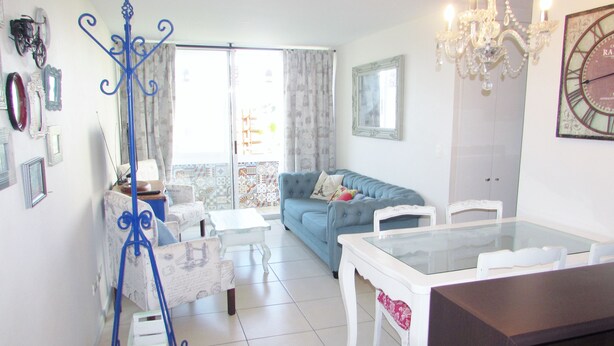A living room with a blue sofa, a white dining table, and a chandelier. - 36.- HNA Paseo Peñuelas (La Serena)