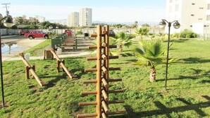 A playground with wooden climbing structures and a small palm tree. - 36.- HNA Paseo Peñuelas (La Serena)