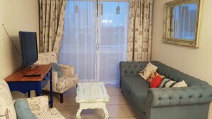 A living room with a sofa, armchair, and a small table with a television. - 36.- HNA Paseo Peñuelas (La Serena)