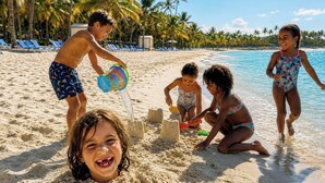 Eine Strandansicht mit spielenden Kindern im Sand, Palmen und klarem, blauem Wasser.