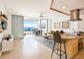 A modern kitchen with a large island, a dining area with a view, and a sliding glass door leading to a balcony.