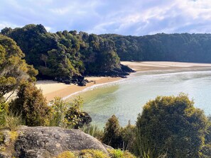 Un paisaje costero con una playa arenosa, aguas claras y colinas con densa vegetación.