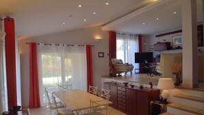 A spacious living area with a dining table, chairs, and a kitchen area with a TV and seating.