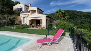 A poolside area with a lounge chair, a swimming pool, and a house with a balcony.