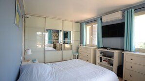 A bedroom with a bed, a dresser, a vanity, a mirror, a TV, and a bookshelf.