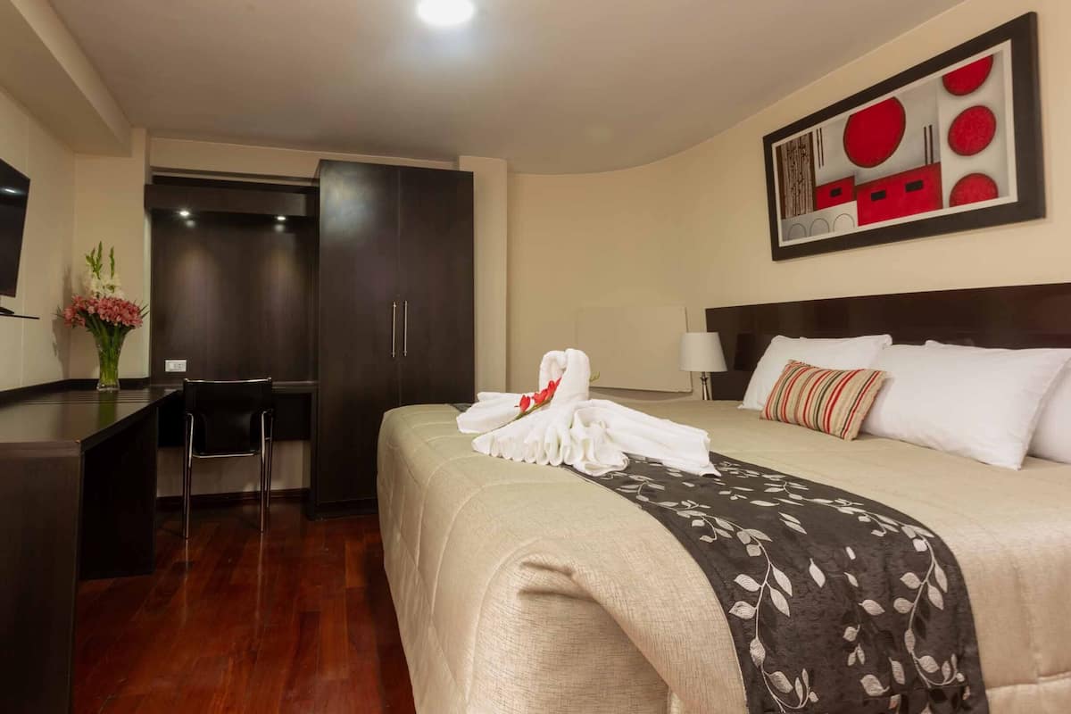 Une chambre d’hôtel avec un lit, un bureau et une chaise. Un vase rempli de fleurs est posé sur le bureau.